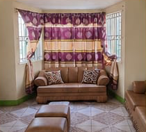 The Eazi Days living room — brown leather sofas, cushions and bright bay windows